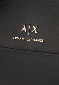 Zwarte faux-lederen oppervlak met een gestructureerde afwerking. Bevat een reliëf gouden logo "A/X ARMANI EXCHANGE" met schone, moderne typografie.