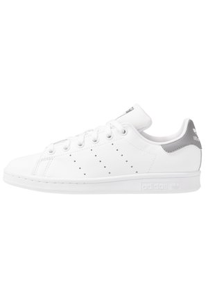 Hvid Adidas Stan Smith sneaker med perforerede striber, hvide snørebånd og grå hælflap, vist i profil på hvid baggrund.