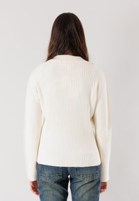Maglione bianco a costine con una vestibilità rilassata, caratterizzato da un colletto discreto e maniche lunghe, abbinato a jeans in denim blu.