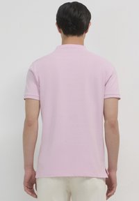 Polo shirt rosa a maniche corte con un design semplice, texture morbida e orlo dritto. Presenta un colletto e spacco laterale per una maggiore comodità.