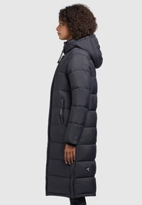 Long, black puffer coat with a hood, featuring a quilted design, zippered pockets, and a snap-button closure at the hem. Smooth texture.