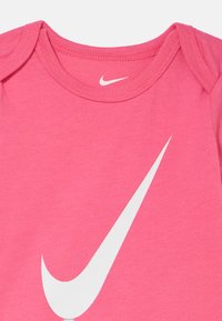 Body rosa de algodão com gola redonda e mangas curtas, com um grande logótipo branco da Nike impresso na frente.