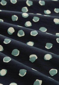 Tissu bleu marine avec une surface texturée présentant des pois teal et blancs de tailles variées, créant un motif ludique.