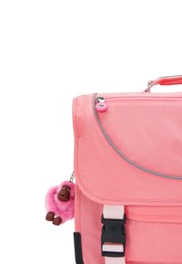 Mochila de tela rosa con cierre de solapa, detalles plateados, correas ajustables y un llavero de monos peludos rosa adjunto.