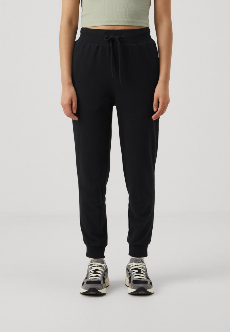 Schwarze Jogginghose mit elastischem Bund und Kordelzug, ausgestattet mit einem schmal zulaufenden Bein-Design. Kombiniert mit gemusterten Sportschuhen.
