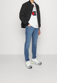 Black bomber jacket, white graphic t-shirt, light blue denim jeans, and gray sneakers with neon accents. Simple, casual look.