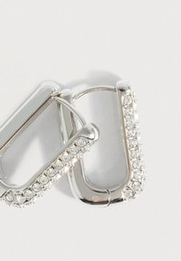 Ασημένια σκουλαρίκια σε σχήμα δαχτυλιδιού με λείος φινίρισμα και διαφάνειες στρας κατά μήκος μιας άκρης. Ο σχεδιασμός είναι ελαφρώς καμπύλος και σύγχρονος.