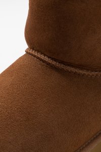 Botină din suede maro, cu detalii țesute la îmbinare, finisaj neted și design minimalist, axat pe confort.