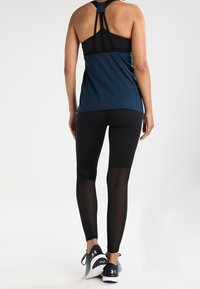 Completo sportivo composto da una canotta turchese e nera con dettagli perforati, abbinata a leggings neri con pannelli testurizzati e scarpe da ginnastica nere.