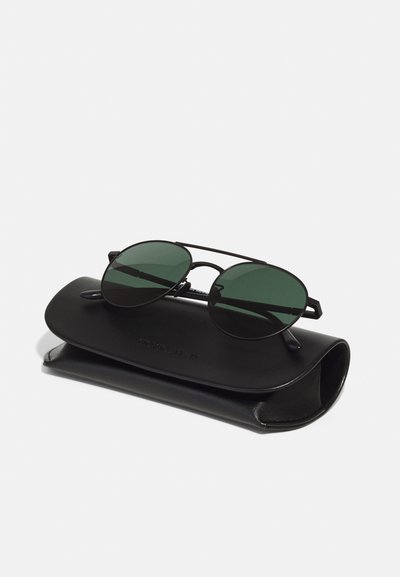 Round black sunglasses with green lenses resting on a black leather case featuring a subtle embossed logo.