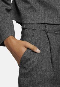 Grijze visgraattextuur stof met een getailleerde pasvorm. Bevat een hoge taille, plooien aan de voorkant en een hand zakelijke zijzak.