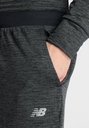 Dark grey athletic pants with a soft texture, elastic waistband, and side pockets. Features a reflective "NB" logo on the lower leg.