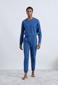 Blå bomulds lounge sæt bestående af en langærmet top med rund hals og bukser med elastiske manchetter, begge designet til komfort og bevægelsesfrihed.