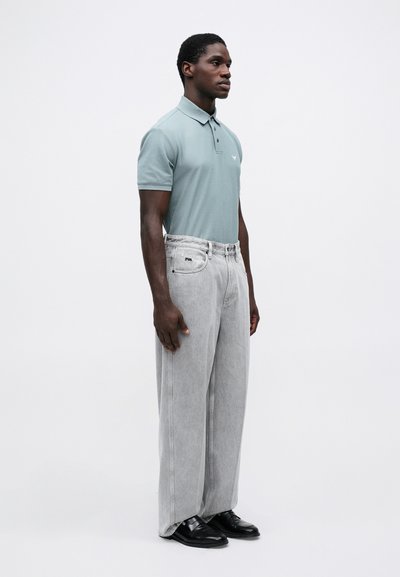 Lyseblå polo-skjorte med krage, kombinert med overdimensjonerte grå denimjeans. Buksene har synlig søm og en logo-lapp.