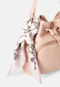 Jasnoróżowa torebka typu bucket z faux leather, z jedwabną chustą związana do uchwytu, z złotym zamkiem błyskawicznym i boczną kieszenią.