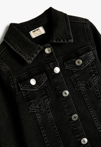 Chaqueta de mezclilla negra con cuello, herrajes plateados, dos bolsillos en el pecho y detalles de costura vertical. La tela parece texturizada y duradera.