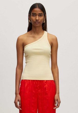 Asymmetrische beige geribde tanktop met een enkele schouderband, gecombineerd met felrode geplooide broeken.