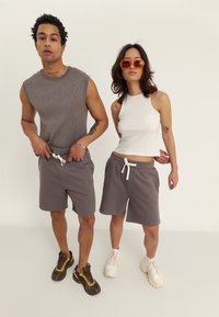 Two models wear casual outfits: a ribbed gray sleeveless top, gray shorts with drawstring, and sneakers. One model has orange sunglasses.