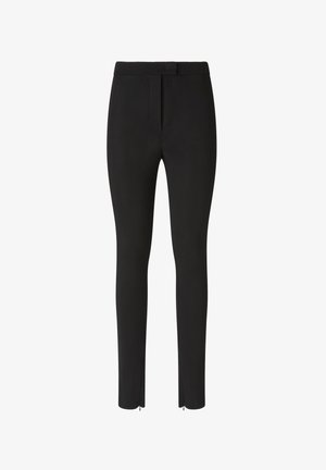 Crne hlače od glatkog, rastezljivog materijala. Imaju uski kroj s pojasom i patentnim zatvaračima na gležnjevima.