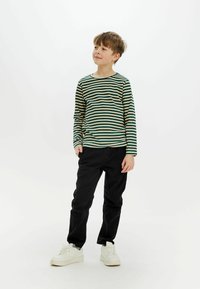 Långärmad skjorta i grön och beige randig design, kombinerad med svarta byxor och vita sneakers. Skjortan har en rund halsringning och ribbad textur.
