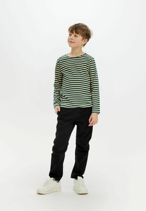 Pitkähihainen, vihreä-beige raidallinen paita, joka on yhdistetty mustiin housuihin ja valkoisiin tennareihin. Paidassa on pyöreä kaula-aukko ja ribbikuviointi.