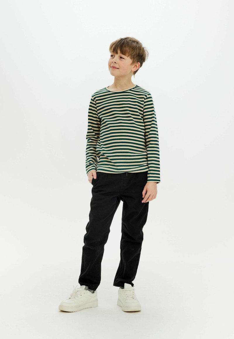 Långärmad skjorta i grön och beige randig design, kombinerad med svarta byxor och vita sneakers. Skjortan har en rund halsringning och ribbad textur.