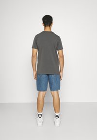 Šedé tričko s krátkým rukávem v kombinaci s modrými džínovými šortkami, nošeno s bílými teniskami a černo-bílými pruhovanými ponožkami. Jednoduchý design, volný střih.