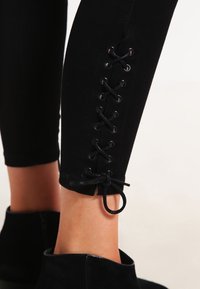 Leggings negros con detalle de cordones en el tobillo, que cuentan con ojales y cordones a juego para ajuste. Textura suave, forma ajustada.
