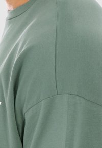 Grøn bomulds-T-shirt med rund hals og korte ærmer, der har en let tekstureret overflade og syninger på skuldrene.