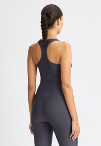 Mörkgrå atletisk tanktop med ribbad struktur och racerback-design, kombinerad med matchande högmidjade leggings. Slätt, figurnära material.