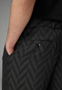 Pantalons noirs à motif présentant un design en chevrons avec des rayures texturées, des poches latérales et une fermeture à bouton au dos de la poche.