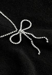 Chaîne en strass argentée formant un nœud sur un fond de tissu noir doux.