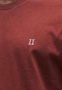 Bordowa bawełniana koszulka z małym, białym haftowanym napisem "II" na piersi, klasycznym okrągłym dekoltem i miękką teksturą.
