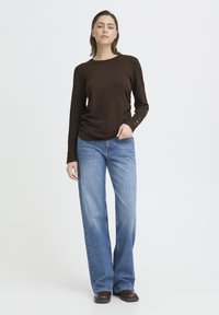 Pruun pika varrukaga topp kergest materjalist, ümmarguse kaelusega ja nööpidega varrukatel, kombineeritud siniste laia säärega teksadega.