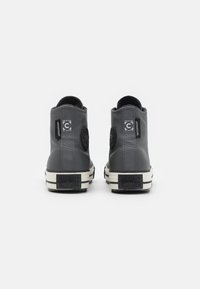 Grijze waterdichte hoge sneakers met rubberen zolen, voorzien van reliëflogo-accenten en contrasterende zwarte labels op de hiel en bovenkant.