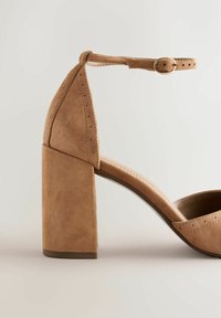 Brauner Wildlederabsatz mit quadratischem Blockdesign, Knöchelriemen und dekorativen Perforationen. Verfügt über ein glattes Innenfutter und eine robuste Sohle.