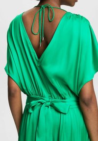 Vestido verde con escote en V en la parte posterior, mangas cortas, cintura elástica y un lazo atado como acento en la cintura. Textura sedosa.