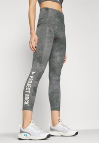 Grey athletic leggings made from textured fabric, featuring a high waistband and "PROJECT ROCK" printed in white on the lower leg.