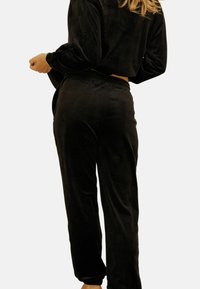 Ensemble de loungewear en velours noir comprenant un haut court à manches longues et un pantalon à taille élastique avec des chevilles ouvertes. Texture douce, design minimal.