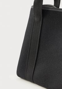 Crna filc torba s teksturiranim, pletenim drškama. Ima čiste linije i ojačane šavove na rubovima za izdržljivost.