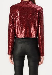 Cropped jacket in burgundy sequin fabric with long sleeves and high collar, paired with black leather pants featuring a smooth texture.