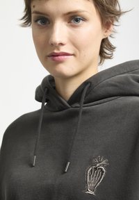 Grijze hoodie met een voorste kangoeroe-zak, trekkoorden en een geborduurd ontwerp met een hartvormig motief in een lichtere tint.