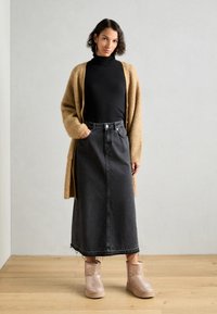 Beige strikket cardigan, svart høyhalset genser, grå denim maxi skjørt, og glitrende rosa ankelstøvler med plattformsåle.