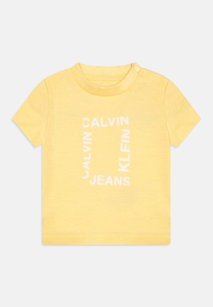 Gelbes T-Shirt mit kurzen Ärmeln und Rundhalsausschnitt, mit einer weißen Grafik von "CALVIN KLEIN JEANS" in einer fett gedruckten Blockschrift.