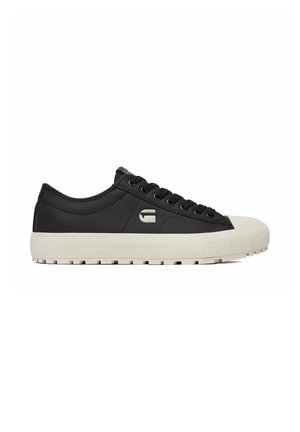 Zapatilla negra de caña baja con suela y puntera de goma blanca, cordones negros y un pequeño logo blanco en el lateral.