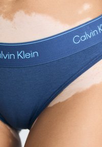 Chiloți din bumbac bleu marin cu un brâu elastic de un bleu deschis, având logo-ul "Calvin Klein", textură netedă și croială de înălțime medie.