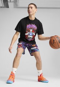 Sort t-shirt med farverigt grafik, lilla pixelmarkerede shorts med mønstre, og multicolore høj-top sneakers, mens der holdes en basketball.