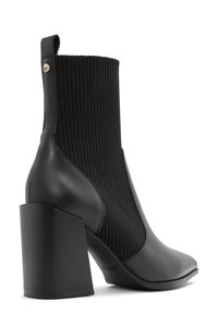 Bottine noire à talons avec un panneau élastique nervuré, en cuir lisse, à bout pointu et à talon géométrique épais.