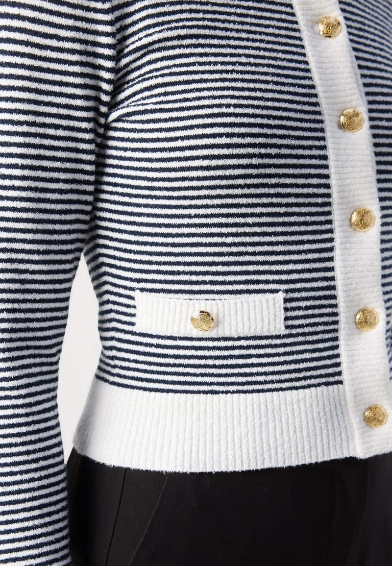 Cardigan rayé bleu marine et blanc avec un tricot texturé, un ourlet côtelé et des boutons dorés à l'avant et sur la poche.