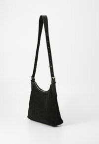 Zwarte suede schoudertas met een zachte textuur, een verstelbare leren schouderband en een zilveren rits aan de bovenkant. Compakt en minimalistisch ontwerp.